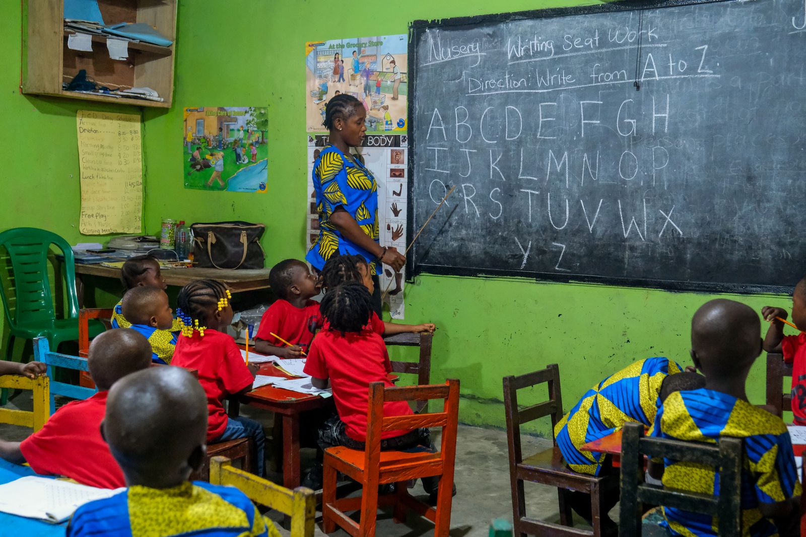 Une enseignante fait la classe devant un tableau avec l'alphabet, entourée d'élèves en uniforme